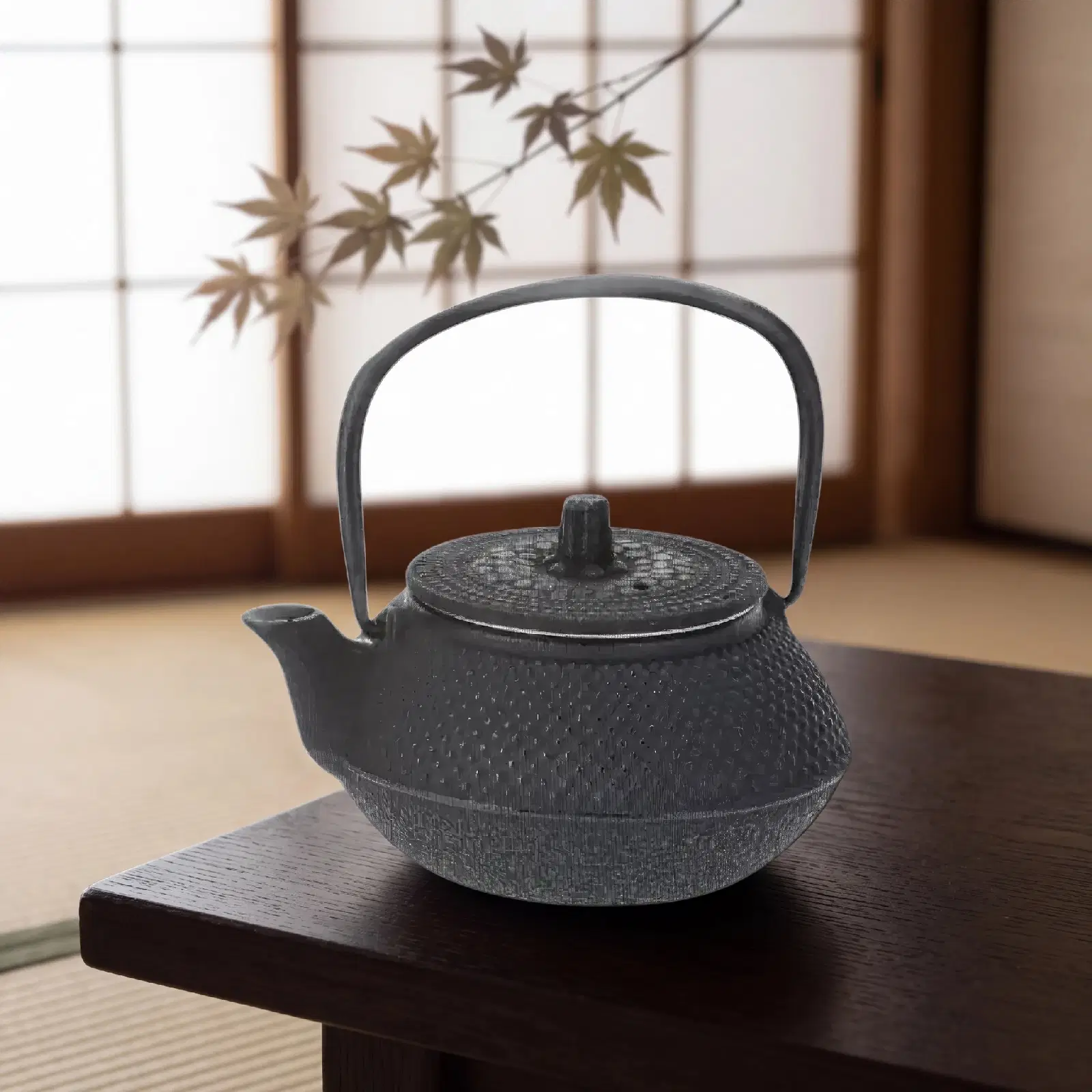 Théière Arare en fonte noire au grain en relief, posée sur une table basse en bois devant une fenêtre japonaise