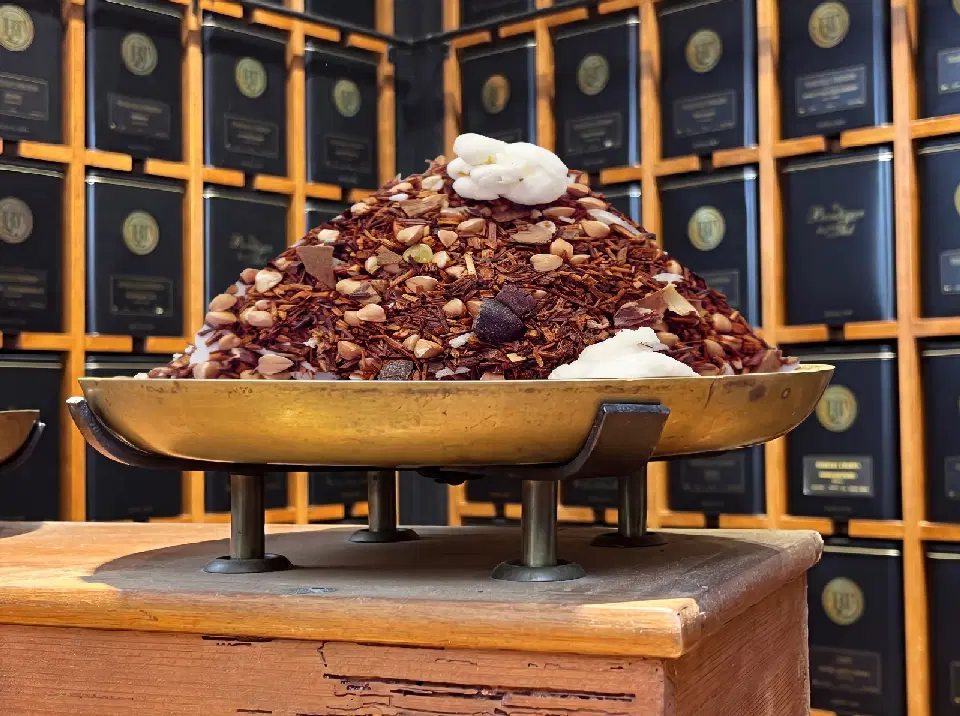 Le Rooibos de Noël Pomme Cannelle Bio en vrac, présenté en dôme sur un plateau doré devant des boîtes à thé