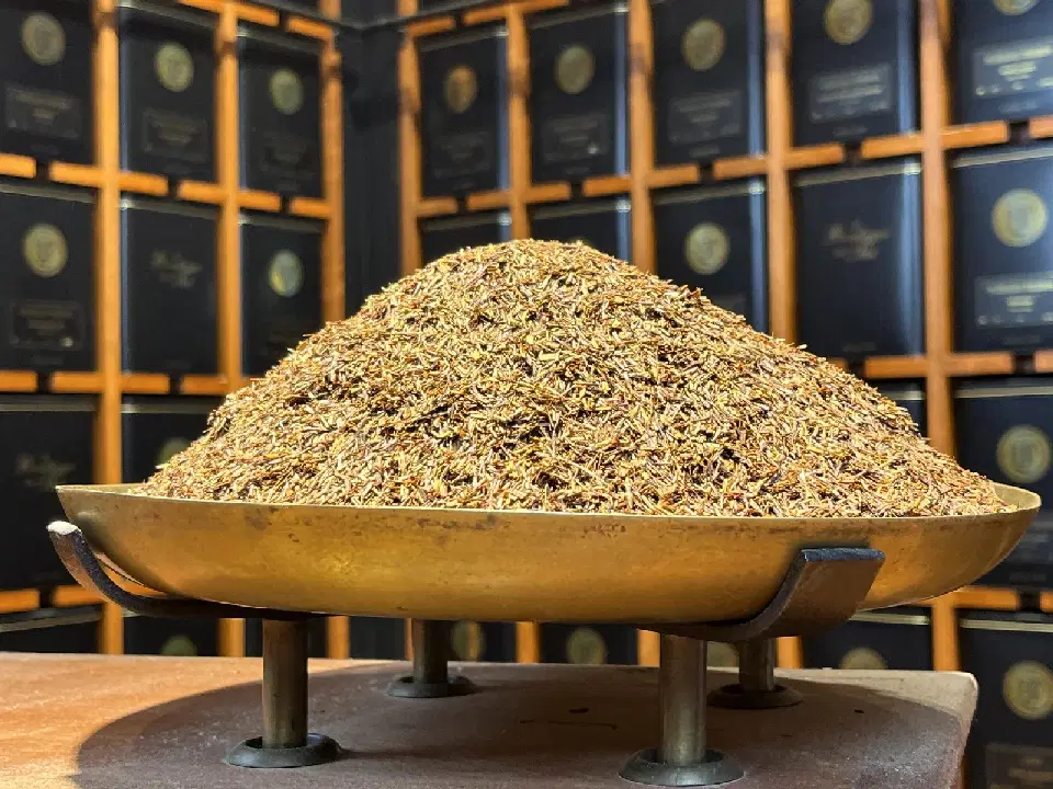 Rooibos Rouge Earl Grey en vrac sur un plateau en laiton, devant des boîtes de thé noires
