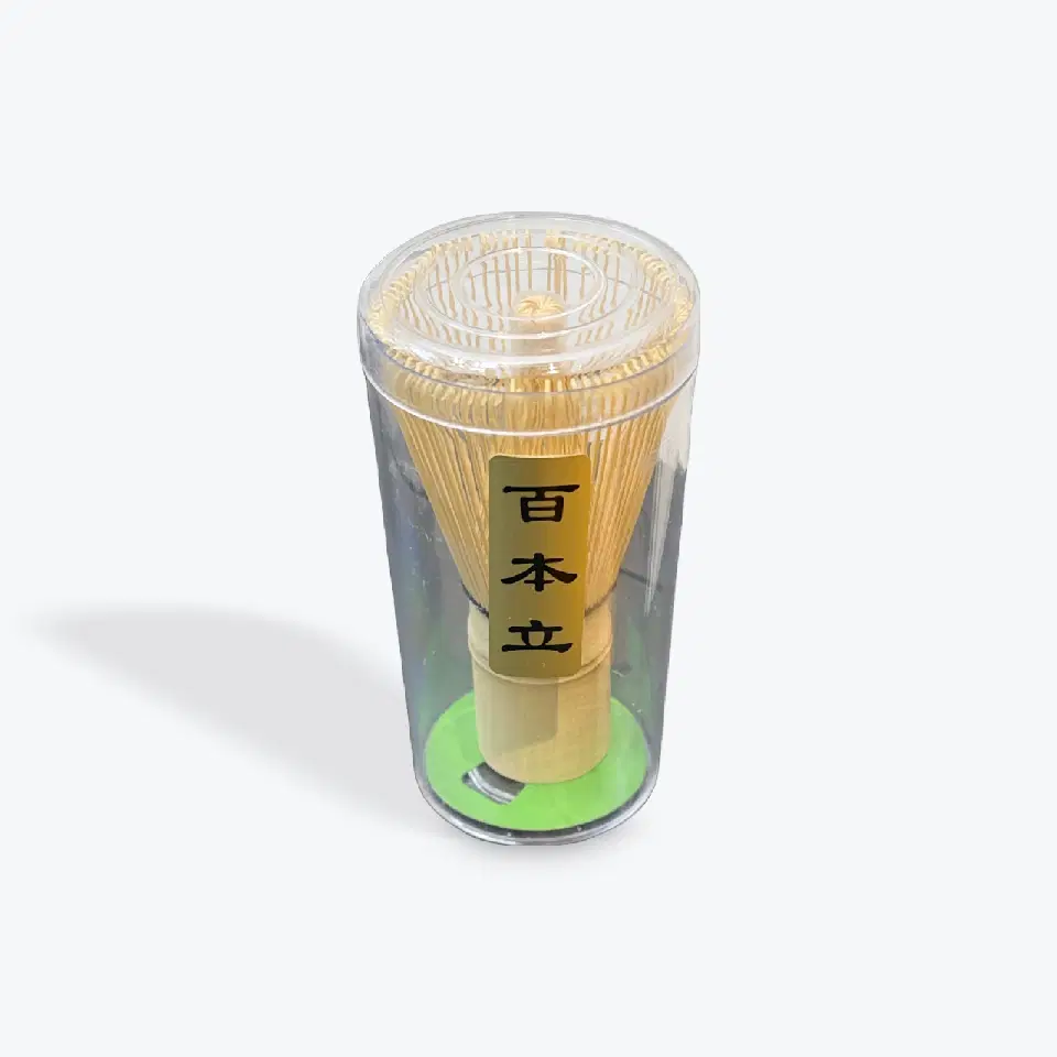 Fouet à matcha en bambou aux brins fins, rangé dans un étui transparent sur un socle vert